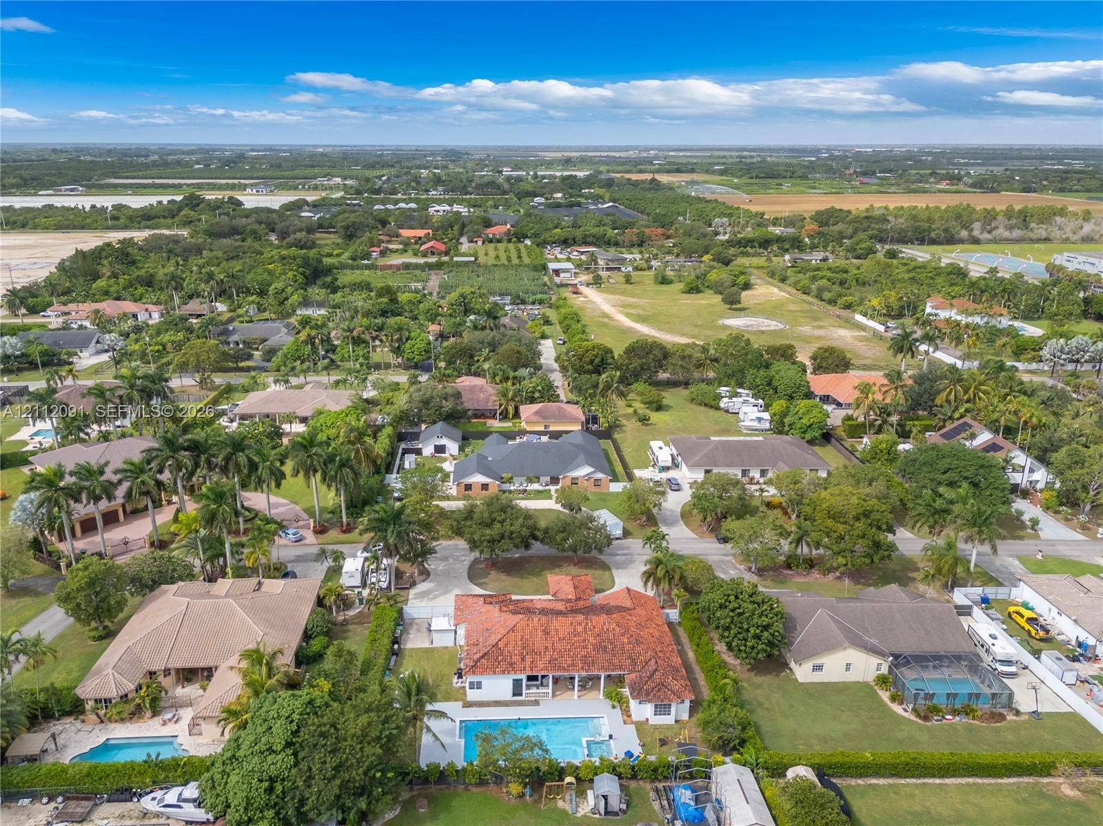 29481 SW 193rd Court, Homestead, FL 33030 Aerial perspective of a residential property featuring a multi-hipped clay tile roof, a rectangular in-ground swimming pool, a concrete patio area, and mature landscaping