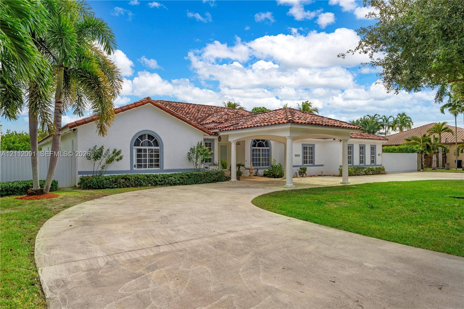 29481 SW 193rd Court, Homestead, FL 33030 Single-story residence featuring a tile roof, arched windows, a covered porte-cochre, and a circular concrete driveway set on a landscaped lot