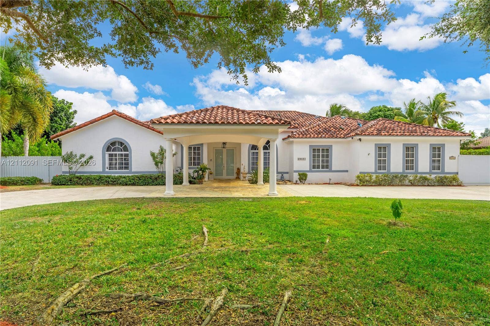 29481 SW 193rd Court, Homestead, FL 33030 Stucco exterior featuring a covered porte-cochre, red tile roofing, arched windows, and a paved circular driveway