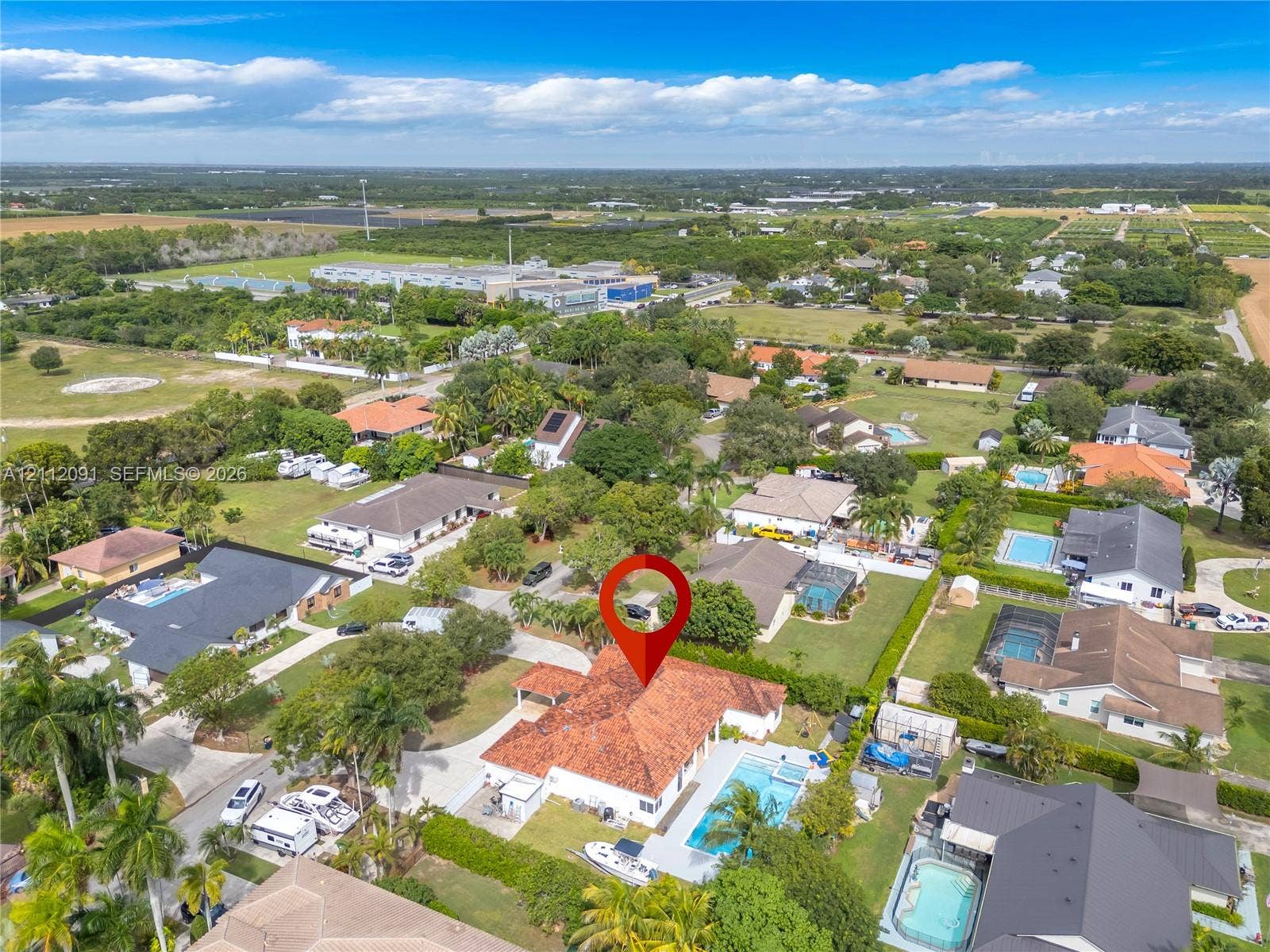 29481 SW 193rd Court, Homestead, FL 33030 Aerial perspective featuring a single-story residence with a multi-hipped terracotta tile roof, an in-ground swimming pool, concrete paved patio area, and mature perimeter landscaping