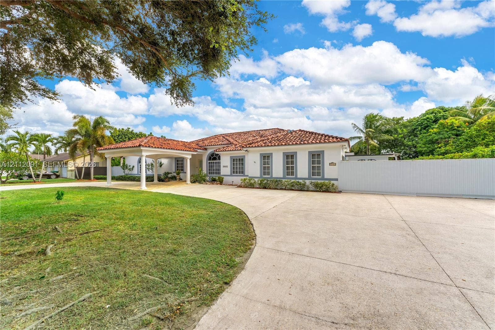 29481 SW 193rd Court, Homestead, FL 33030 Single-story residence featuring a clay tile roof, covered porte-cochre, multi-pane windows, expansive concrete motor court, and perimeter privacy fencing