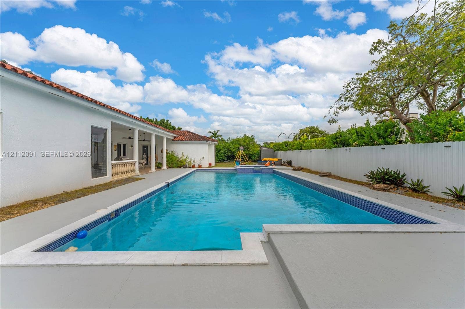 29481 SW 193rd Court, Homestead, FL 33030 In-ground swimming pool with tile border, expansive concrete decking, covered patio with structural columns, and perimeter privacy fencing