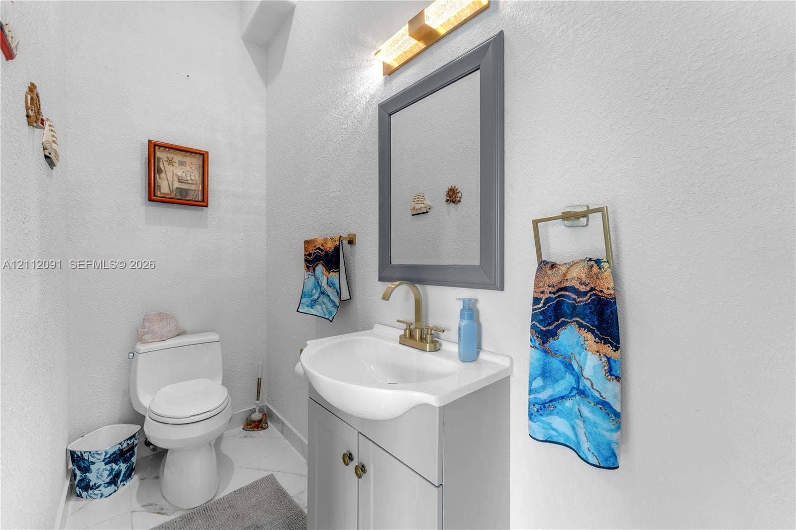 29481 SW 193rd Court, Homestead, FL 33030 Grey vanity cabinet with a white basin, brass-finish faucet, framed wall mirror, modern linear wall-mounted lighting, and tile flooring