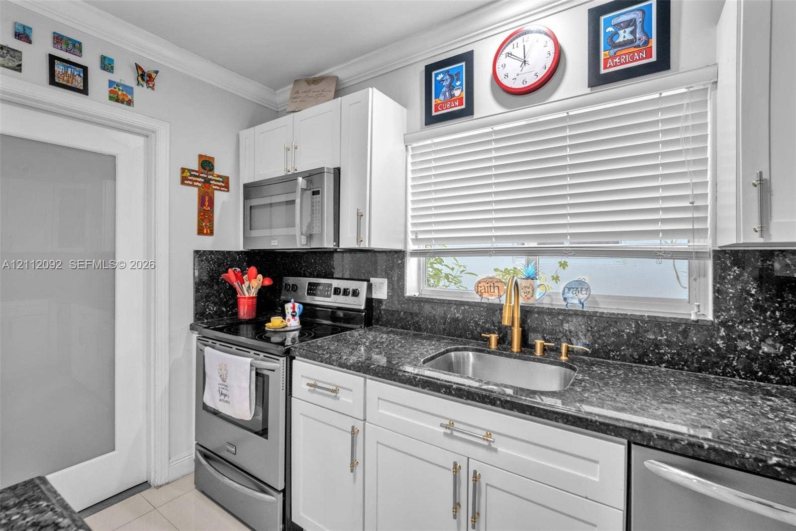 419 Sevilla Avenue, Coral Gables, FL 33134 Kitchen featuring white shaker-style cabinetry, dark stone countertops, stainless steel appliances, a brass-toned gooseneck faucet, and a frosted glass panel door