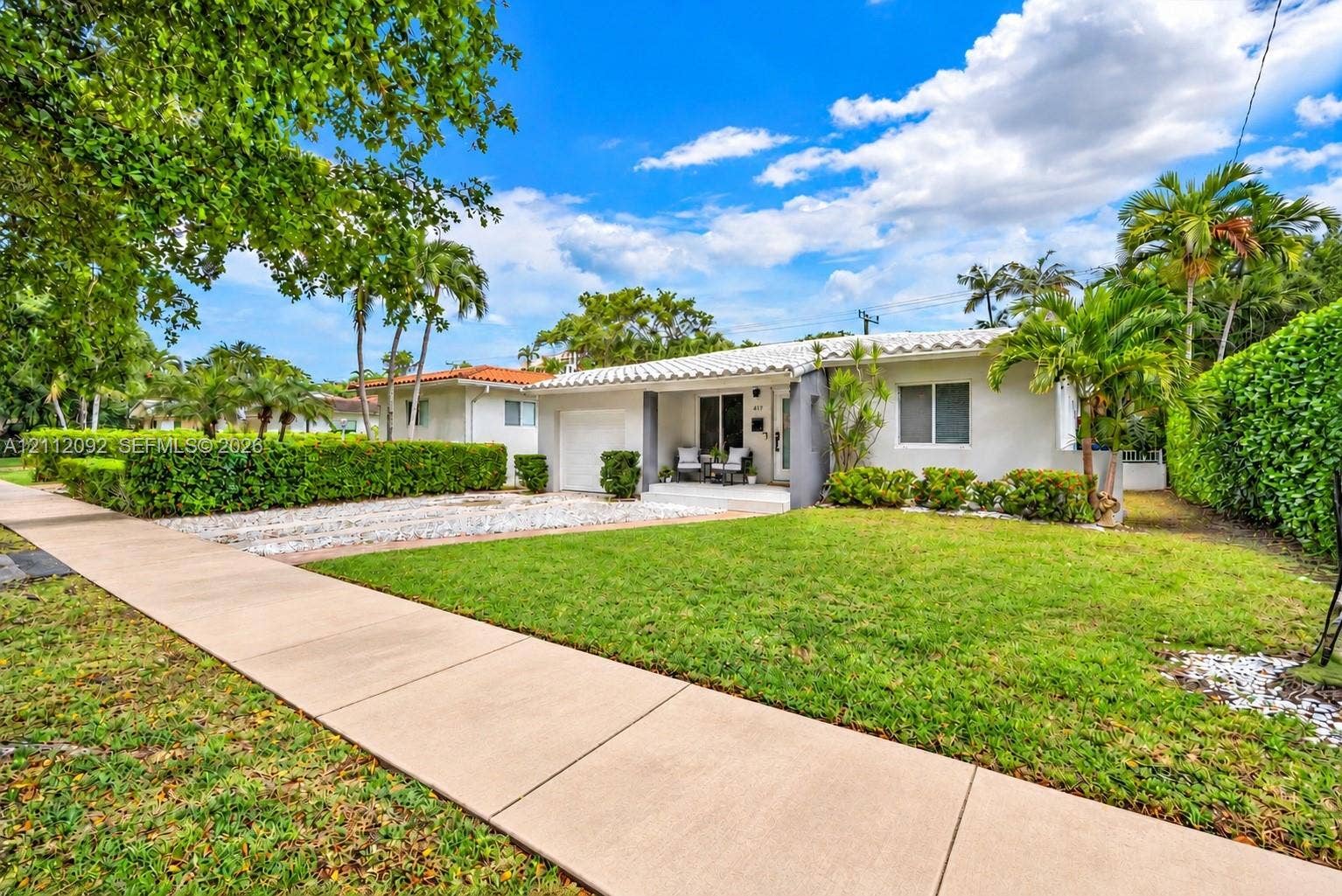 419 Sevilla Avenue, Coral Gables, FL 33134 Single-story residence featuring a barrel tile roof, white stucco exterior, attached garage, stone-surfaced driveway, and landscaped shrubbery
