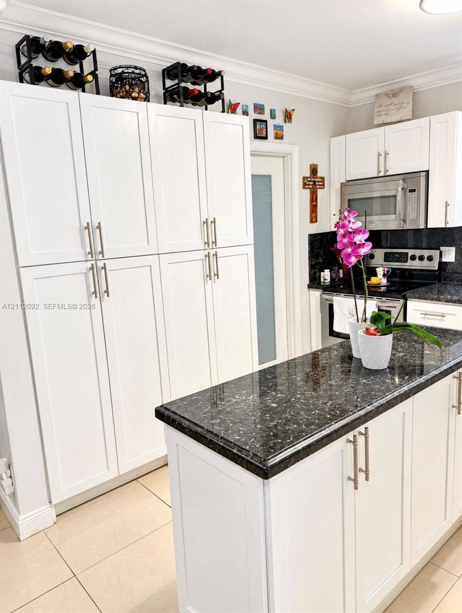 419 Sevilla Avenue, Coral Gables, FL 33134 Kitchen featuring white shaker-style cabinetry, a central island with a stone-finish countertop, stainless steel microwave, integrated oven, and tile flooring