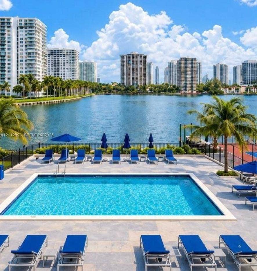 2750 NE 183rd Street, #1612, Aventura, FL 33160 In-ground swimming pool featuring a stone-paver deck, metallic pool ladder, and perimeter fencing, set against a waterfront backdrop