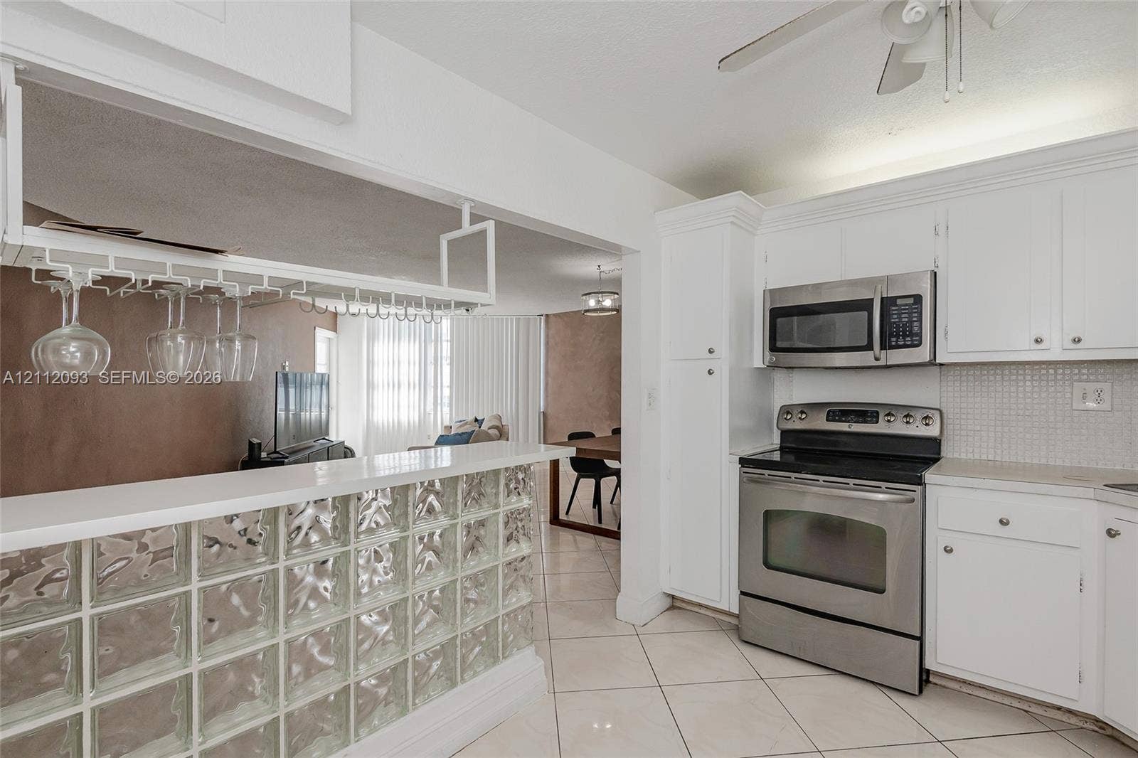 2750 NE 183rd Street, #1612, Aventura, FL 33160 Kitchen featuring white cabinetry, stainless steel appliances, a glass block peninsula, and an overhead stemware rack