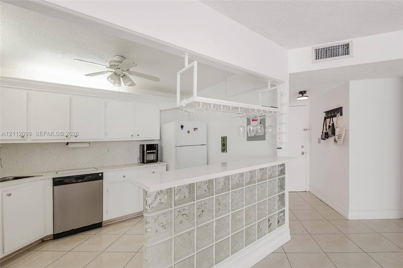 2750 NE 183rd Street, #1612, Aventura, FL 33160 Kitchen featuring white cabinetry, solid-surface breakfast bar with a glass block base, overhead stemware rack, and tile flooring