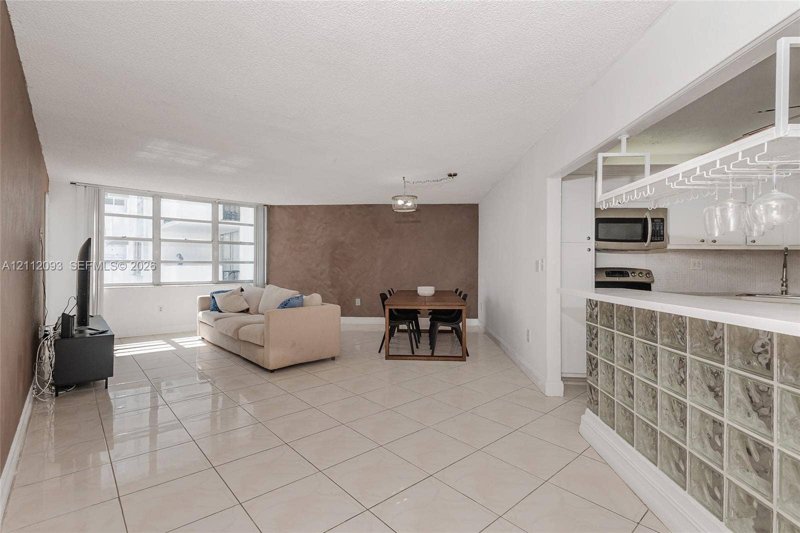 2750 NE 183rd Street, #1612, Aventura, FL 33160 Open-concept interior featuring large-format tile flooring, a glass block breakfast bar, an integrated hanging glass rack, and expansive windows
