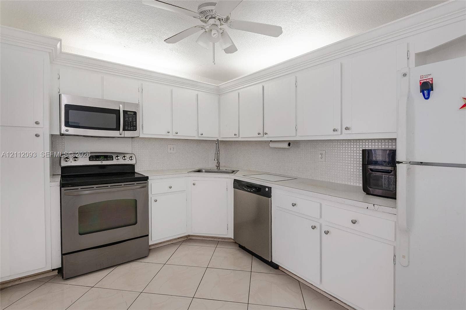 2750 NE 183rd Street, #1612, Aventura, FL 33160 Kitchen featuring white cabinetry with crown molding, stainless steel appliances, tiled backsplash, and ceramic tile flooring