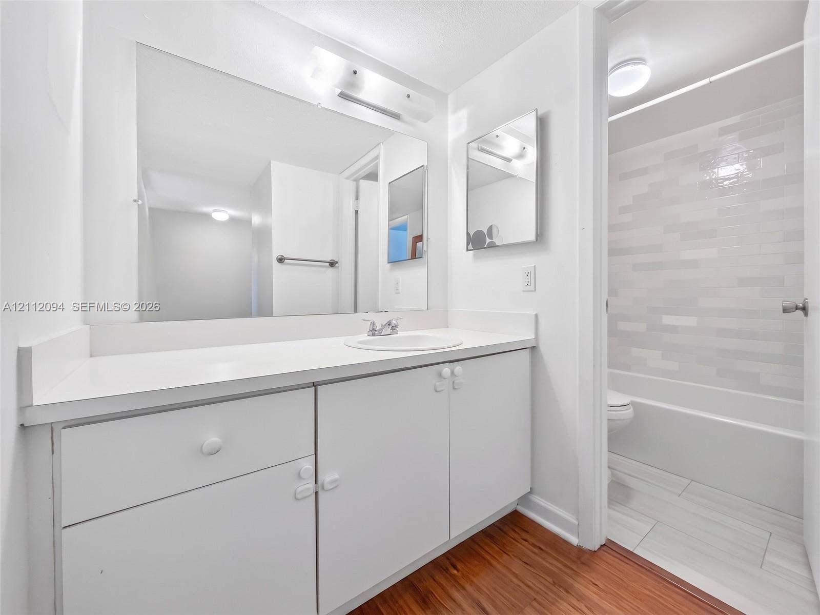 4600 SW 67th Avenue, #242, Miami, Miami, FL 33155 Bathroom featuring a vanity with a white countertop and integrated sink, large wall-mounted mirror, wood-finish flooring, and a bathtub with tile surround