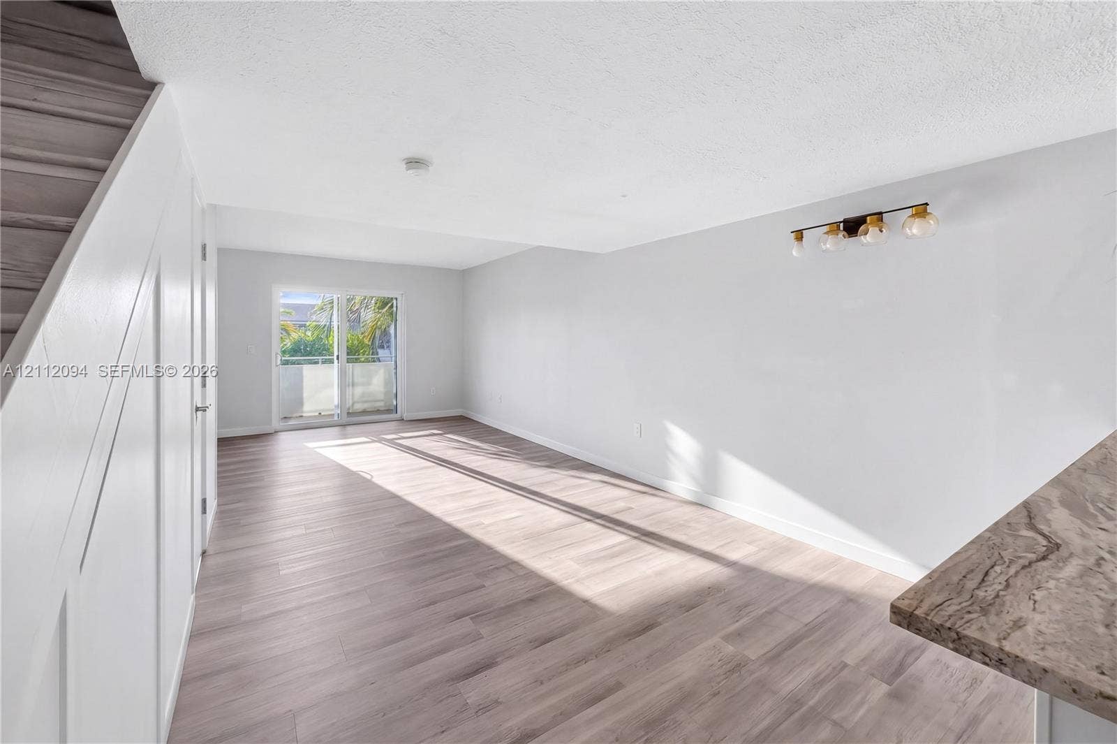 4600 SW 67th Avenue, #242, Miami, Miami, FL 33155 Open-concept interior featuring wood-finish flooring, sliding glass patio doors, stone-finish countertops, and multi-bulb wall lighting