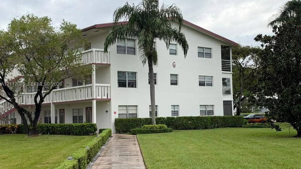 256 Fanshaw G, #2560, Boca Raton, FL 33434 Multi-level exterior with white stucco facade, stacked balconies, tiled walkway, and mature landscaping