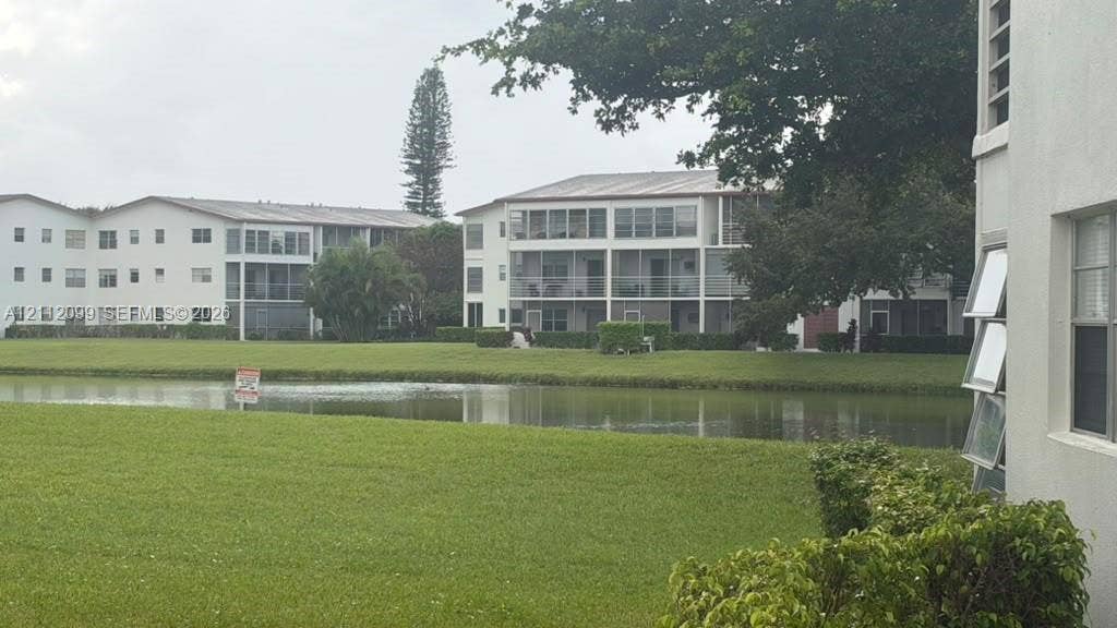 256 Fanshaw G, #2560, Boca Raton, FL 33434 Multi-story residential buildings featuring screened-in lanais, light-toned exterior finish, expansive common area lawn, and pond frontage