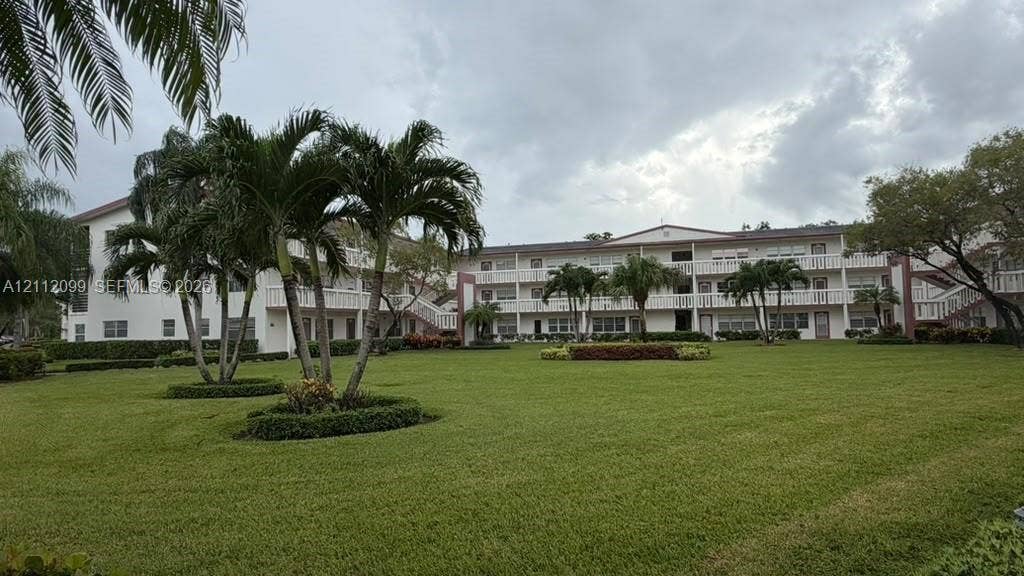 256 Fanshaw G, #2560, Boca Raton, FL 33434 Multi-level exterior featuring a light-toned stucco faade, open-air balcony railings, expansive manicured lawn, and mature palm tree landscaping