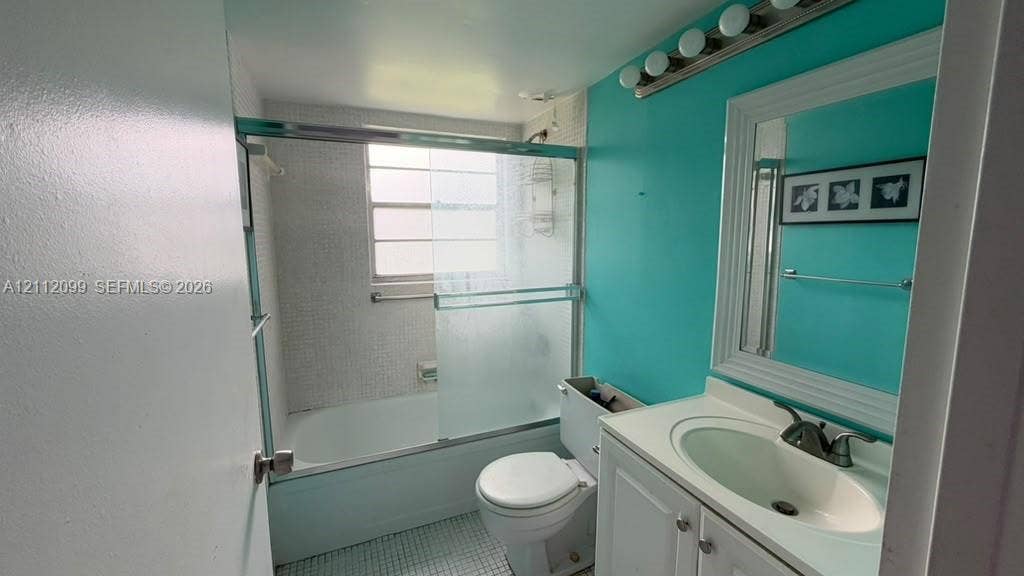 256 Fanshaw G, #2560, Boca Raton, FL 33434 Bathroom featuring a white vanity cabinet with an integrated sink, polished metal faucet, a framed wall mirror, a bathtub with sliding glass doors, and a tiled shower surround