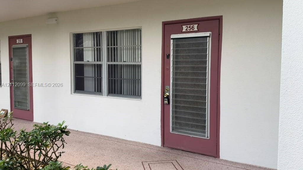 256 Fanshaw G, #2560, Boca Raton, FL 33434 Exterior entrance featuring a solid door with a full-length security screen, dual-pane window with vertical blinds, and a smooth stucco finish