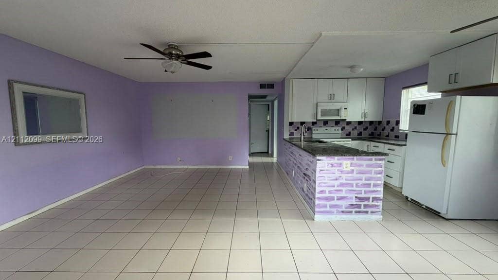 256 Fanshaw G, #2560, Boca Raton, FL 33434 Kitchen featuring white cabinetry, stone-finish countertops, a tiled backsplash, and a peninsula with brick-style detailing, complemented by tile flooring throughout
