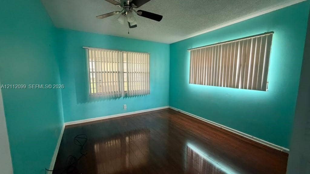 256 Fanshaw G, #2560, Boca Raton, FL 33434 Room featuring wood-finish flooring, two sets of windows with vertical blinds, and a multi-blade ceiling fan with light fixture