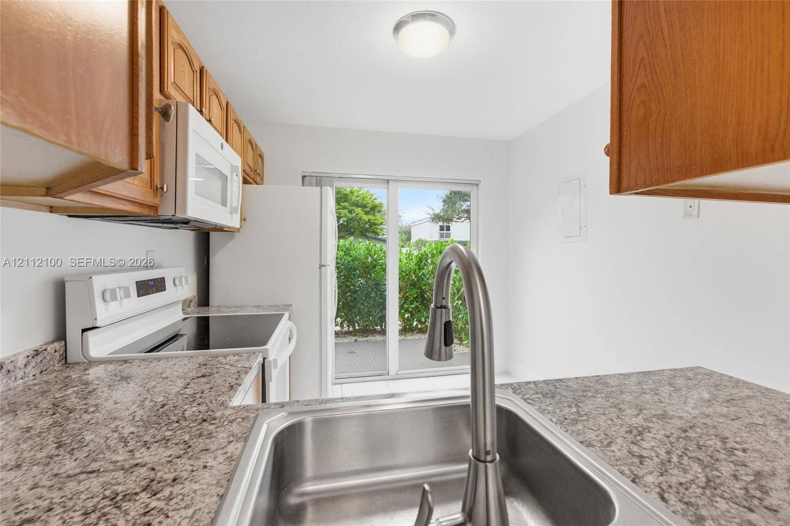 3003 NW 5th Terrace, #1, Pompano Beach, Pompano Beach, FL 33064 Kitchen featuring speckled laminate countertops, stainless steel undermount sink with a high-arch pull-down faucet, wood-finish cabinetry, white appliances, and a glass sliding door
