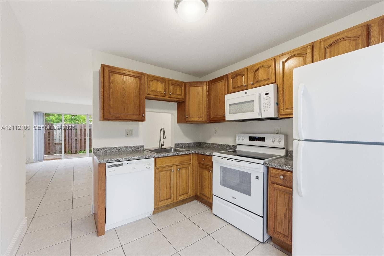 3003 NW 5th Terrace, #1, Pompano Beach, Pompano Beach, FL 33064 Kitchen featuring wood cabinetry, stone-patterned laminate countertops, tile flooring, and white appliances including a range, microwave, and dishwasher