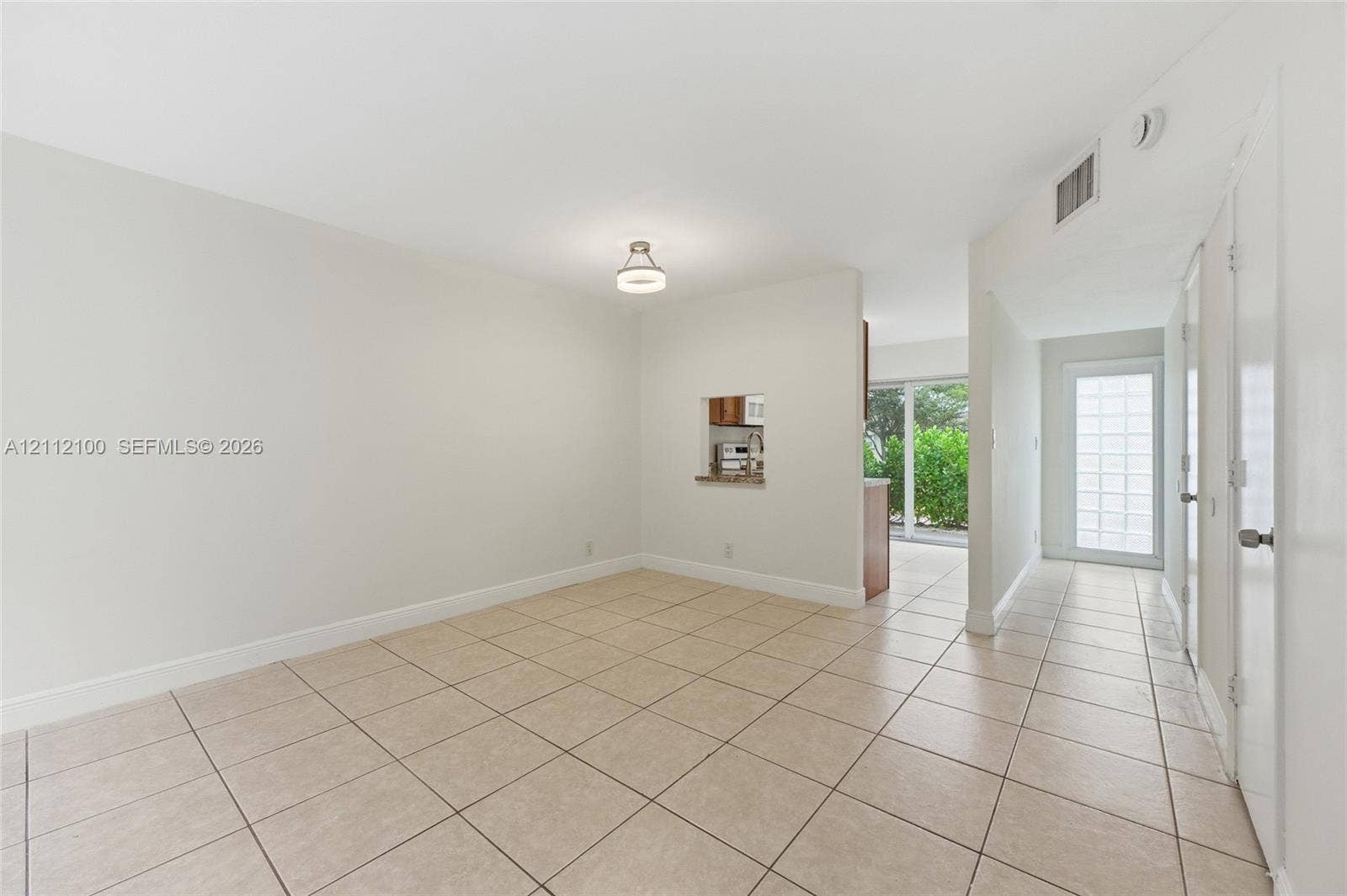 3003 NW 5th Terrace, #1, Pompano Beach, Pompano Beach, FL 33064 Neutral-toned interior space featuring light-colored ceramic tile flooring, a pass-through window to the kitchen, a contemporary flush-mount ceiling fixture, and a glass-paneled exterior door
