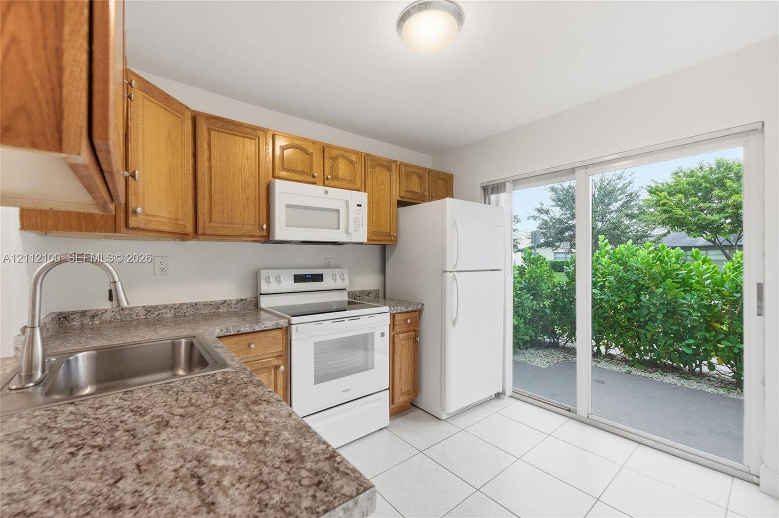 3003 NW 5th Terrace, #1, Pompano Beach, Pompano Beach, FL 33064 Kitchen featuring wood cabinetry, stone-finish countertops, stainless steel sink with high-arch faucet, white appliances, and a sliding glass door