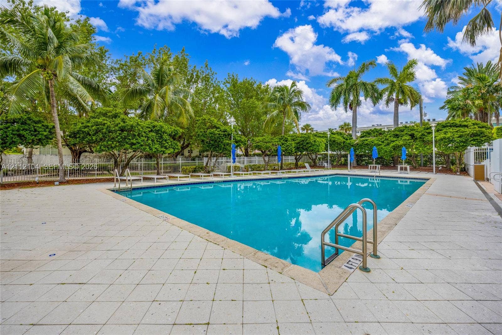 7900 Harbor Island Drive, #1203, North Bay Village, North Bay Village, FL 33141 Swimming pool with light-toned tiled deck, metal handrails, and surrounding perimeter fencing set amidst mature landscaping and palm trees