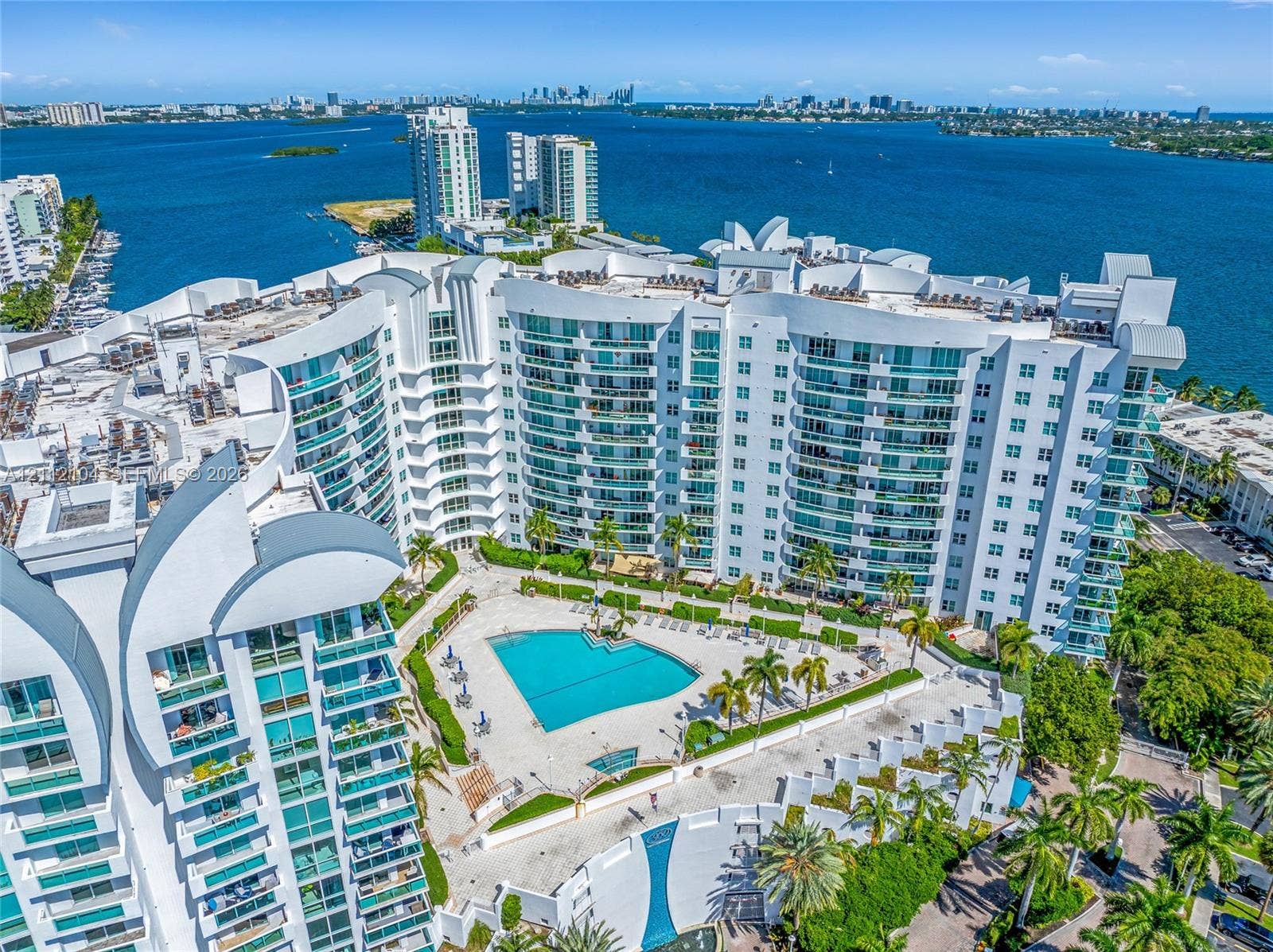7900 Harbor Island Drive, #1203, North Bay Village, North Bay Village, FL 33141 High-rise residential exterior featuring expansive glass balconies, an outdoor swimming pool, manicured landscaping, and direct waterfront access