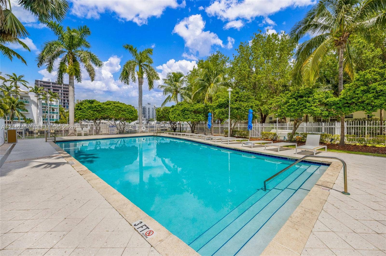 7900 Harbor Island Drive, #1203, North Bay Village, North Bay Village, FL 33141 In-ground swimming pool featuring a light-toned stone deck, built-in entry steps, stainless steel handrail, and surrounding mature palm trees