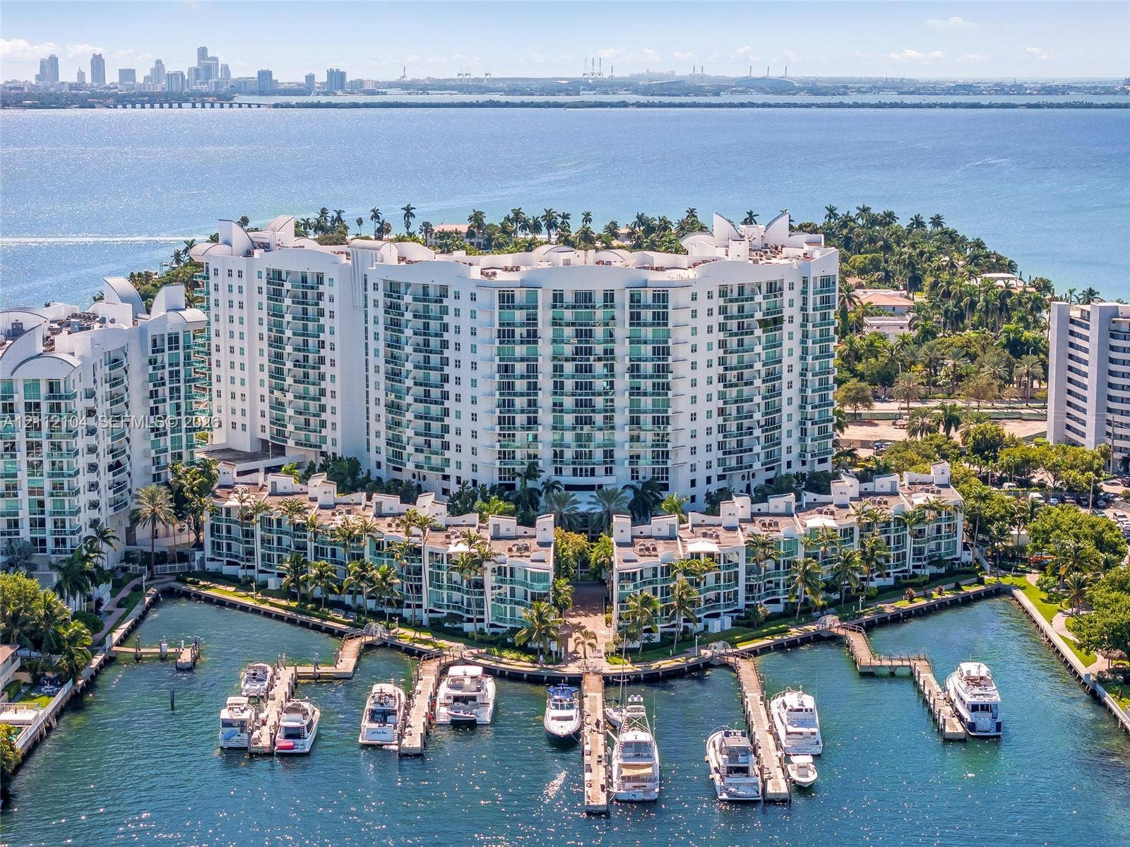 7900 Harbor Island Drive, #1203, North Bay Village, North Bay Village, FL 33141 Waterfront condominium complex featuring high-rise architecture, private boat slips, balconies with glass railings, landscaped grounds, and a cityscape backdrop
