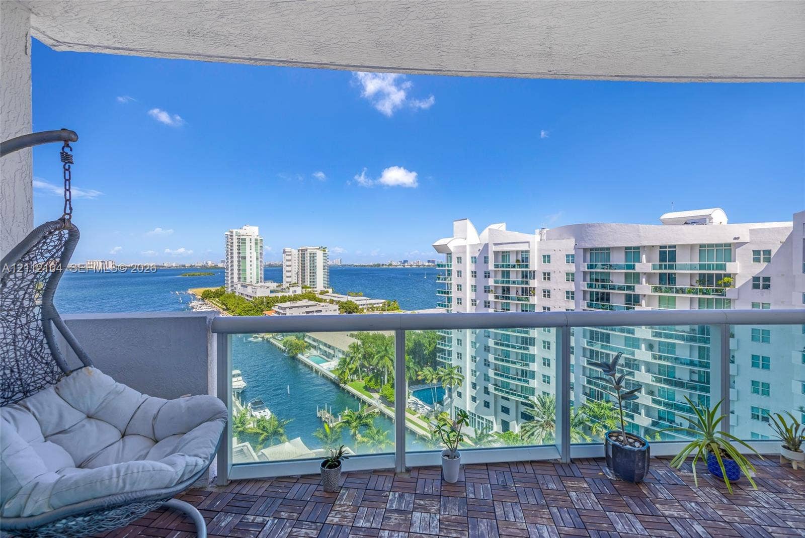 7900 Harbor Island Drive, #1203, North Bay Village, North Bay Village, FL 33141 Covered balcony featuring wood-finish deck tiling and a glass-panel railing, overlooking water and urban scenery