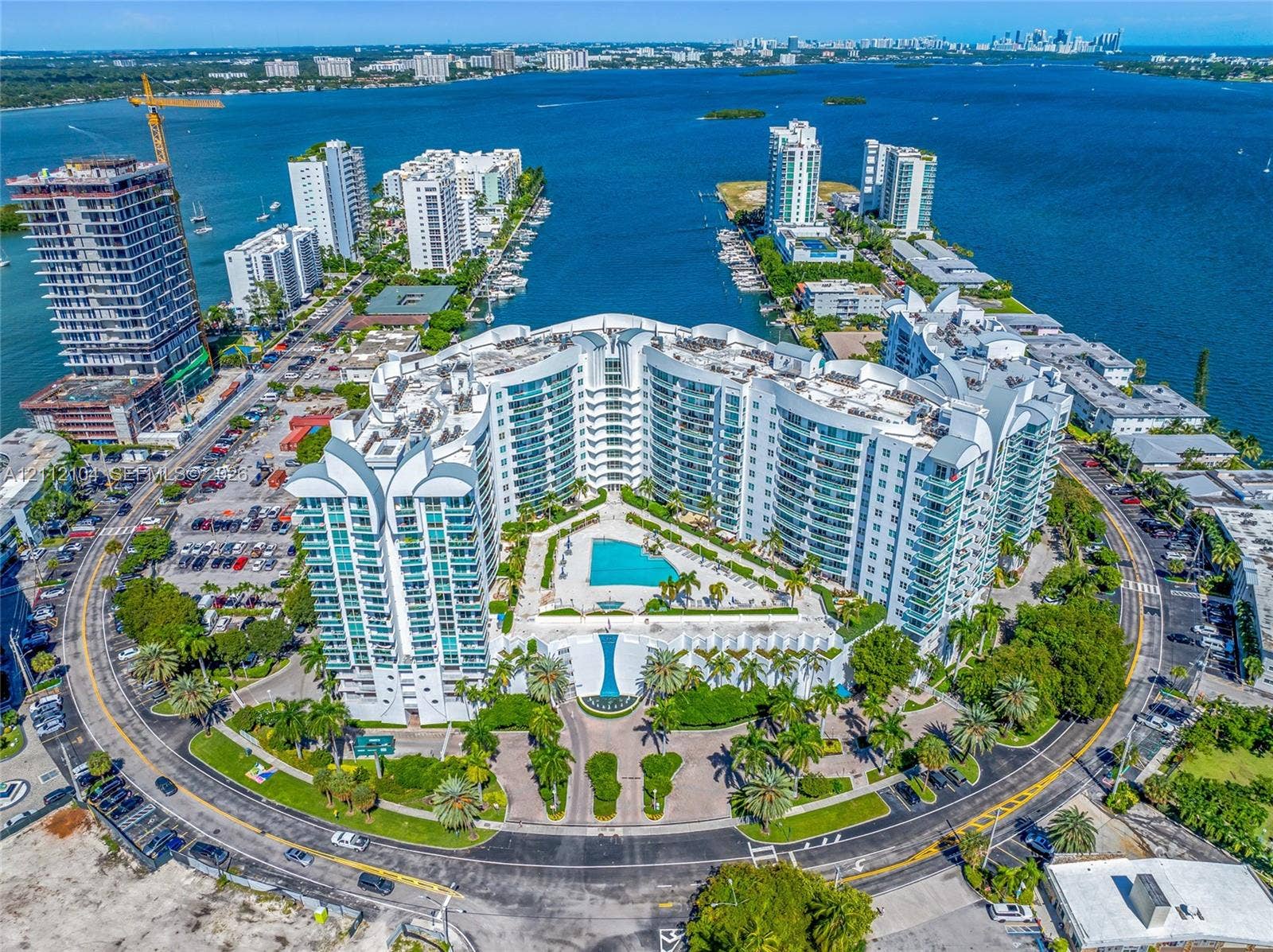 7900 Harbor Island Drive, #1203, North Bay Village, North Bay Village, FL 33141 Waterfront residential complex featuring tiered glass-paneled architecture, a central swimming pool with sun deck, landscaped grounds with palm trees, and gated circular drive access