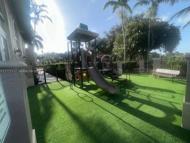 1209 NE 32nd Avenue, Homestead, Homestead, FL 33033 Outdoor recreation area featuring artificial turf, a permanent playground structure with a slide, built-in metal bench seating, and perimeter metal fencing