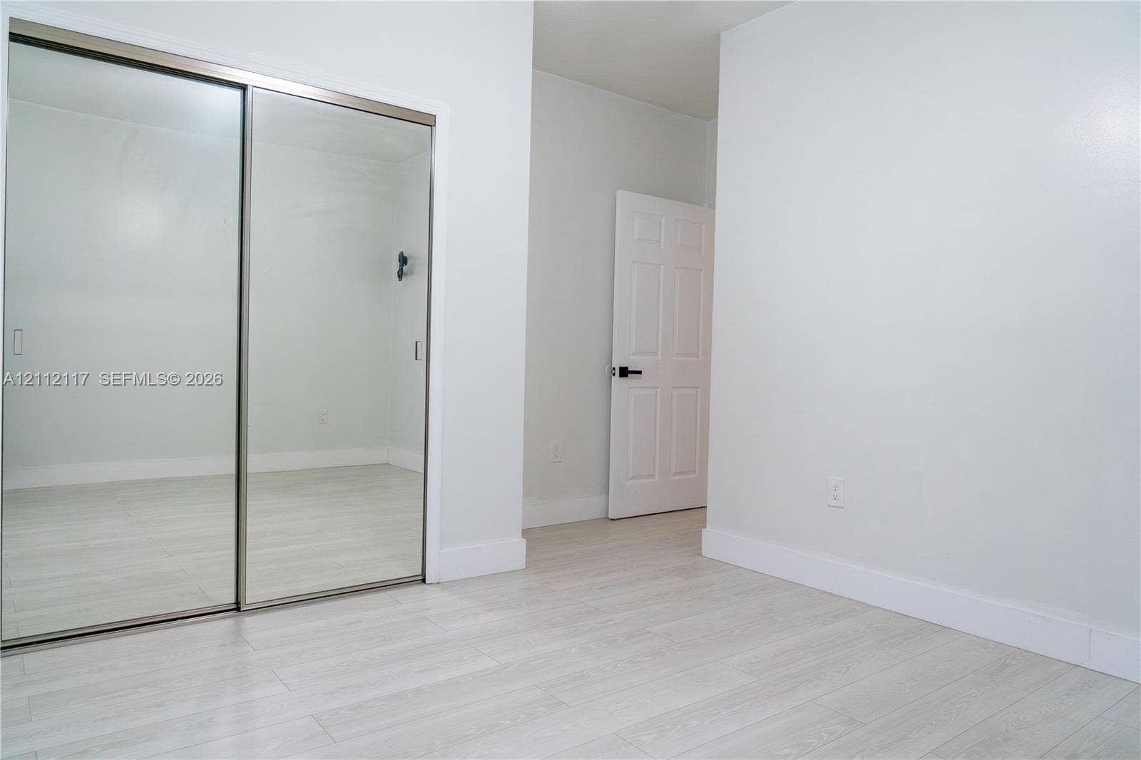 1209 NE 32nd Avenue, Homestead, Homestead, FL 33033 Sliding mirror-panel closet doors, light-toned wood-finish flooring, and a solid-core interior door with matte black hardware