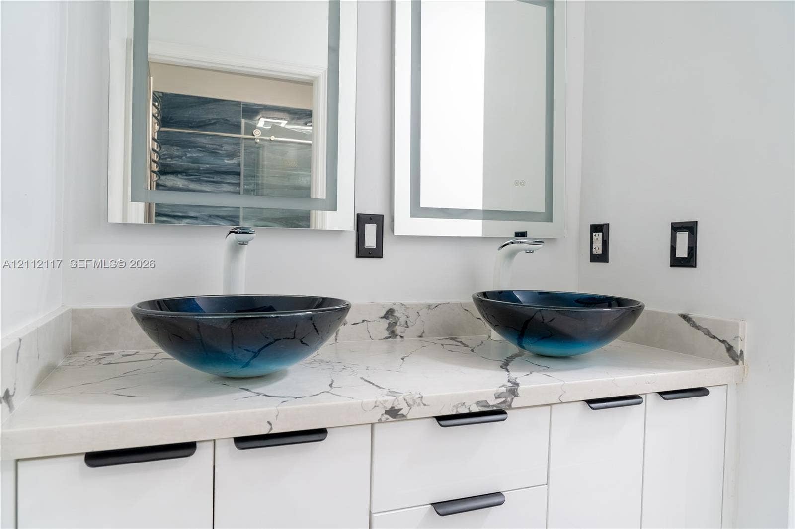 1209 NE 32nd Avenue, Homestead, Homestead, FL 33033 Dual-sink vanity featuring stone-patterned countertops, integrated vessel sinks, white cabinetry with matte black pulls, and illuminated wall-mounted mirrors