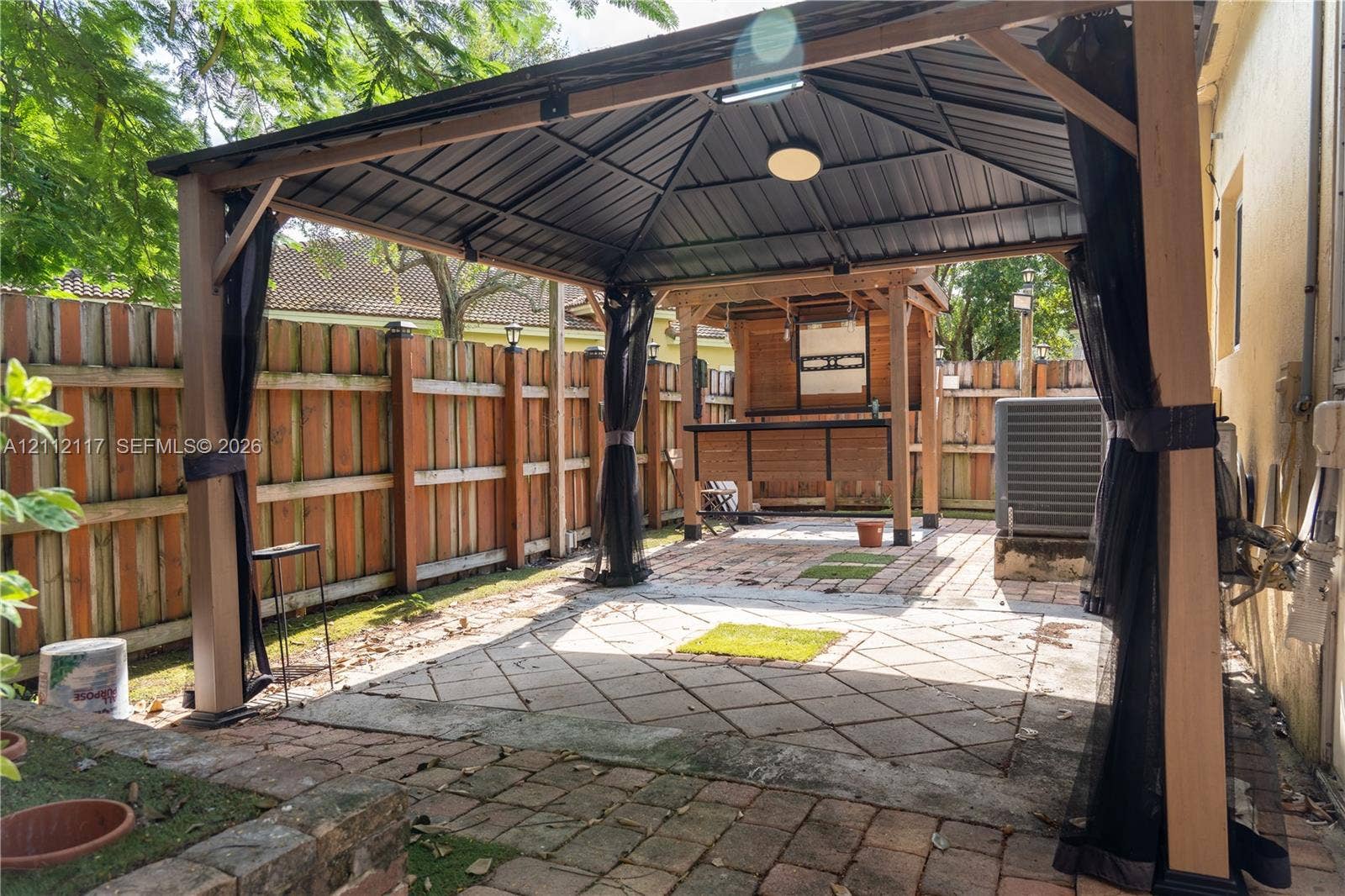 1209 NE 32nd Avenue, Homestead, Homestead, FL 33033 Outdoor patio area featuring a metal-frame gazebo, paved stone surfaces, and wood-panel privacy fencing