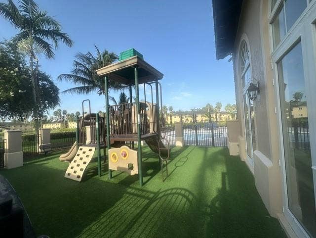 1209 NE 32nd Avenue, Homestead, Homestead, FL 33033 Outdoor space featuring synthetic turf, fixed play structure, arched glass-paned double doors, and exterior wall-mounted light fixtures