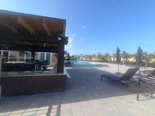 1209 NE 32nd Avenue, Homestead, Homestead, FL 33033 Covered outdoor kitchen featuring a stone-topped bar, wood-beamed ceiling, stone paver patio, and swimming pool