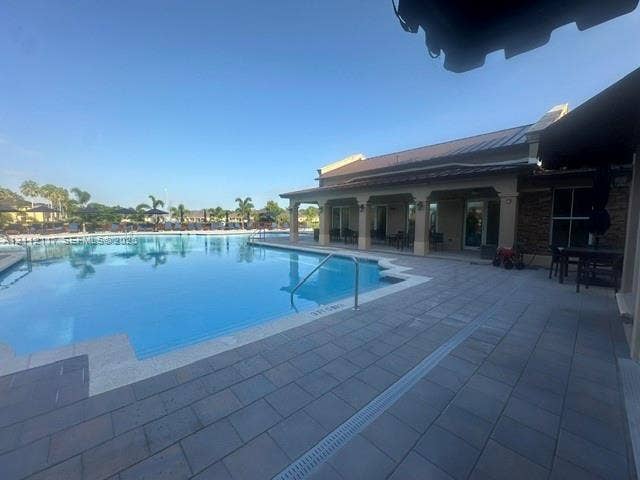 1209 NE 32nd Avenue, Homestead, Homestead, FL 33033 In-ground swimming pool featuring a tiled deck, covered patio, metal roof, and stone masonry exterior accents