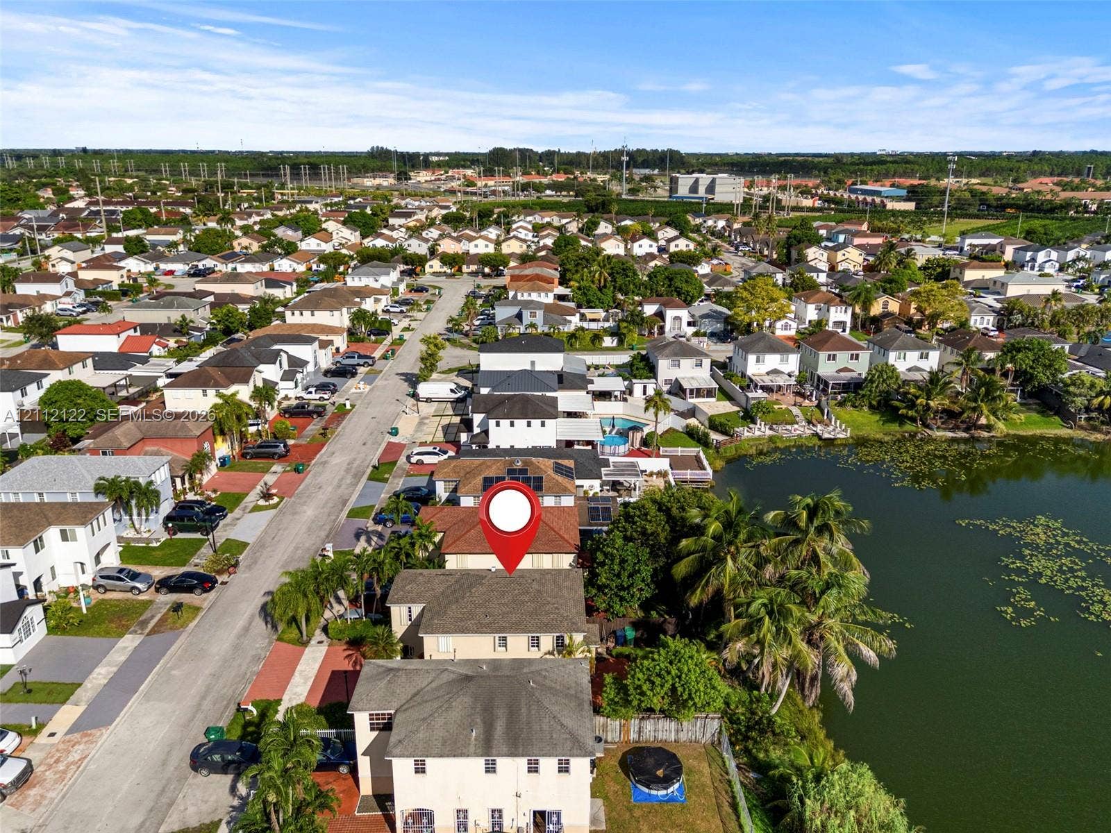 13990 SW 161st Terrace, Miami, FL 33177 Aerial perspective of a multi-story residence featuring solar panels, a concrete tile roof, and a fenced rear yard bordering a natural lake