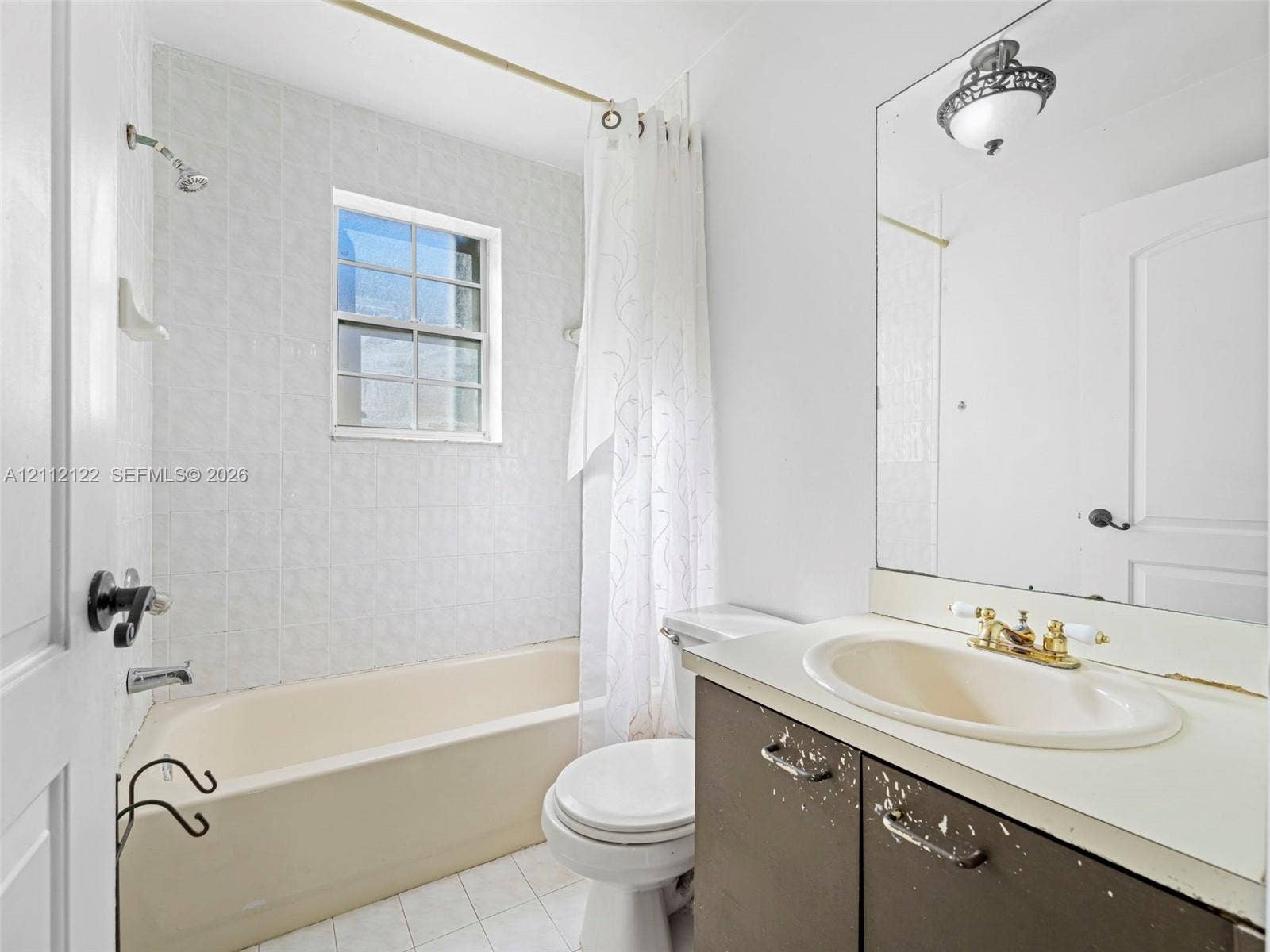 13990 SW 161st Terrace, Miami, FL 33177 Full-width wall mirror, bathtub with a tiled surround, recessed window, and vanity with an integrated basin and metallic finish hardware
