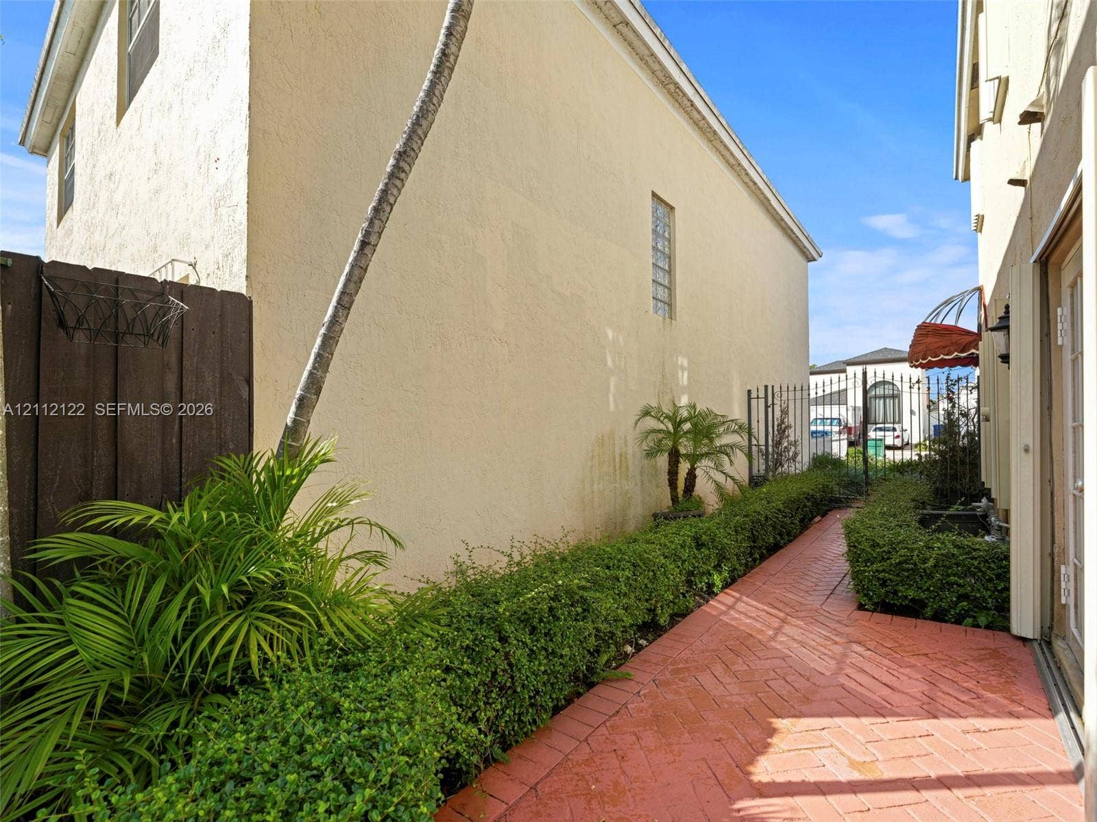 13990 SW 161st Terrace, Miami, FL 33177 Side exterior featuring herringbone brick paving, mature manicured shrubbery, stucco siding, and a vertical glass block accent window