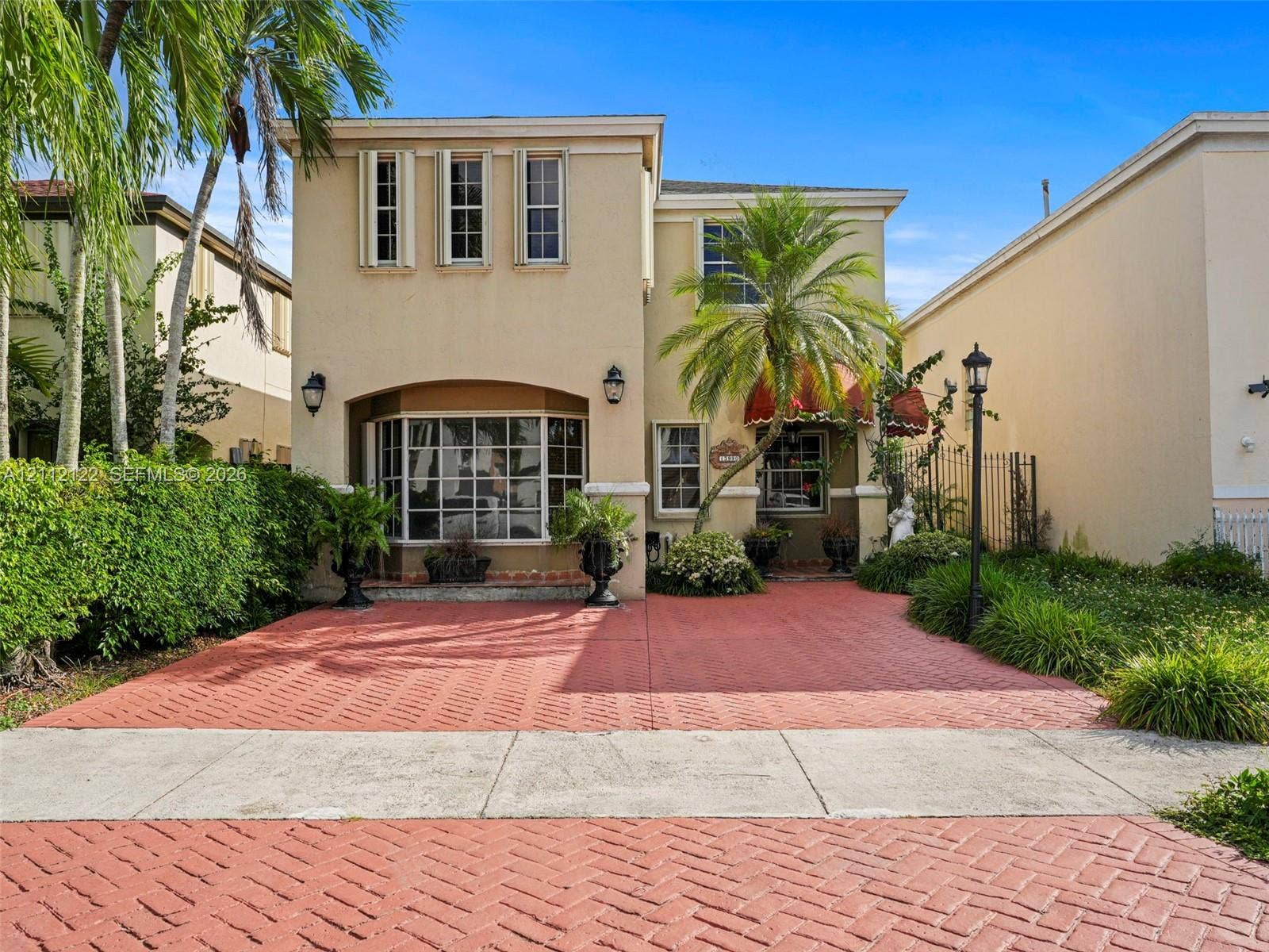 13990 SW 161st Terrace, Miami, FL 33177 Two-story exterior featuring a stucco faade, herringbone-patterned paved driveway, bay window, and arched entryway with decorative awning