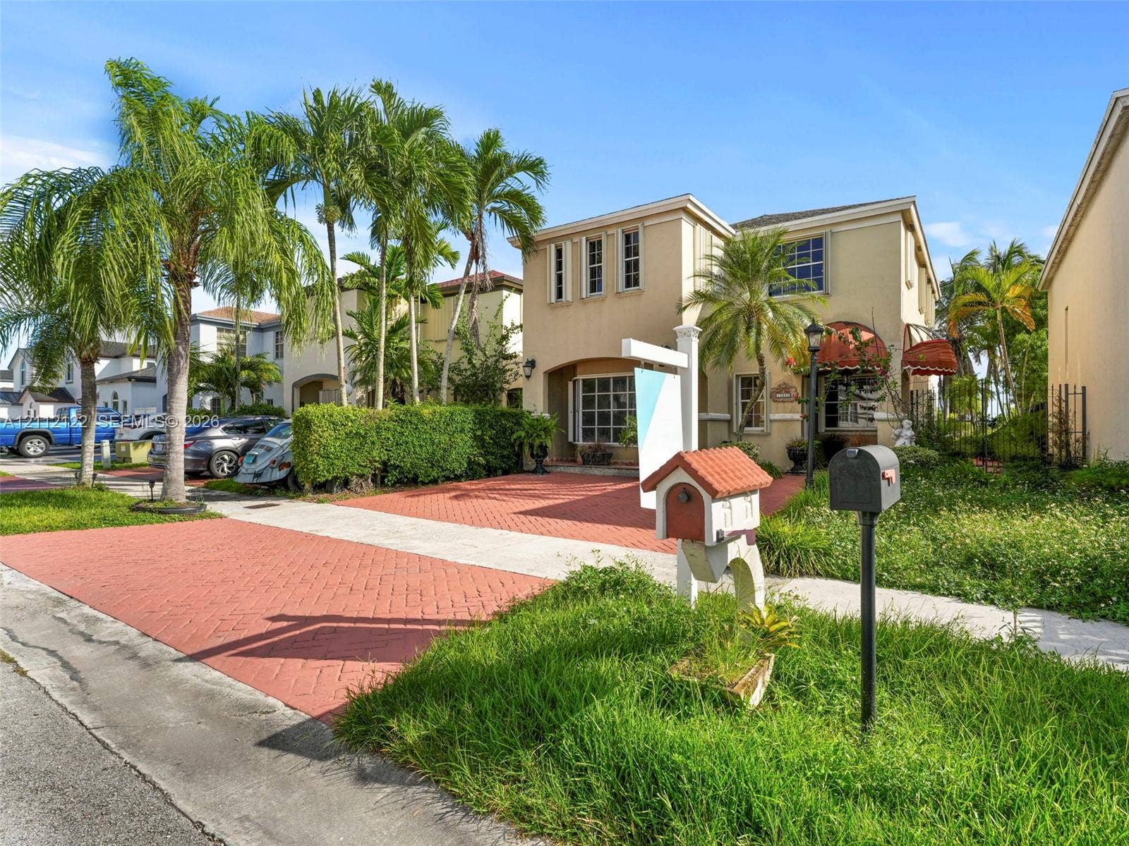 13990 SW 161st Terrace, Miami, FL 33177 Two-story stucco exterior featuring a red brick-patterned driveway, multi-pane bay window, and custom decorative awnings