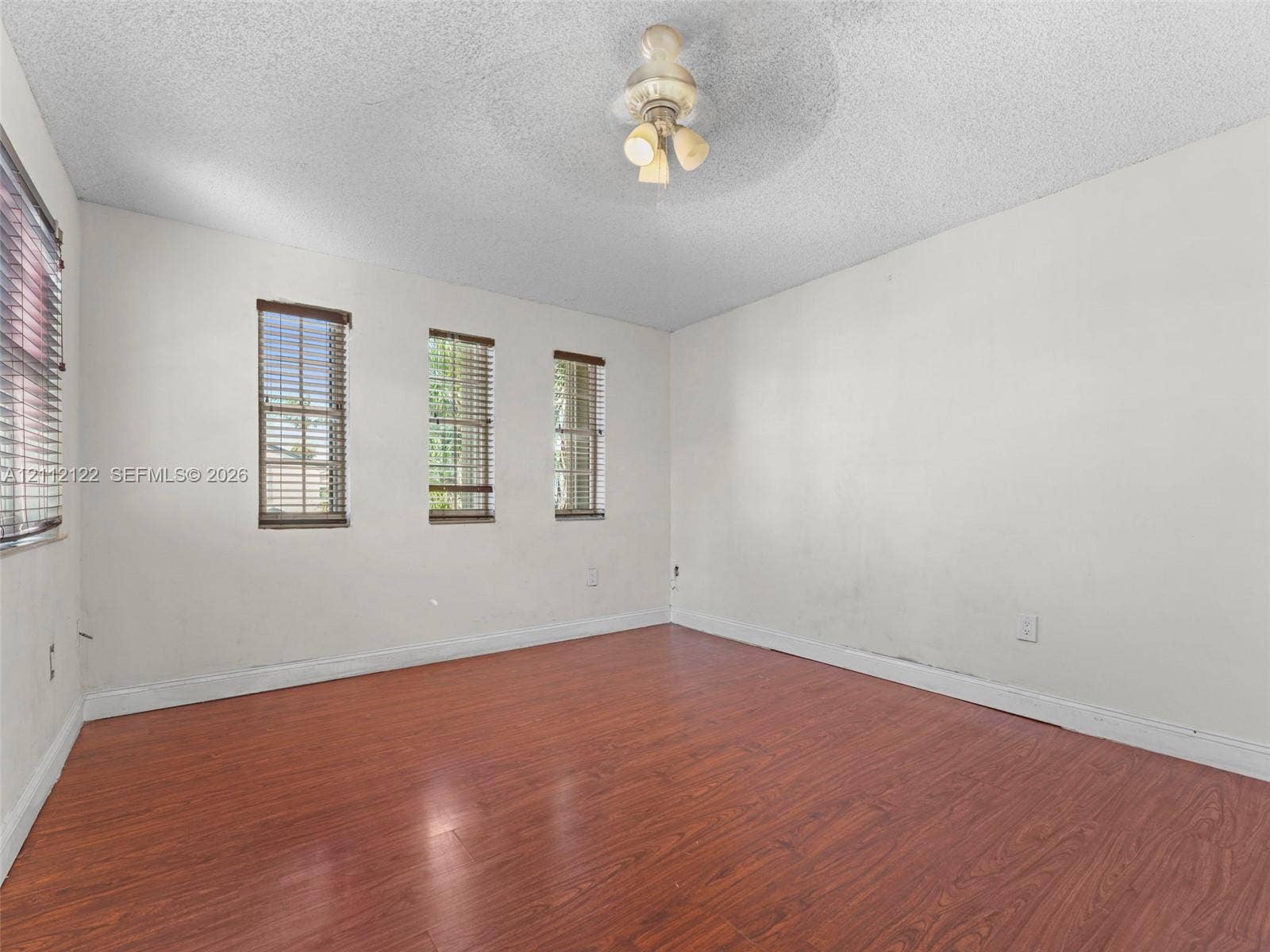 13990 SW 161st Terrace, Miami, FL 33177 Wood-finish flooring, three vertical windows with horizontal blinds, and a central ceiling-mounted light fixture