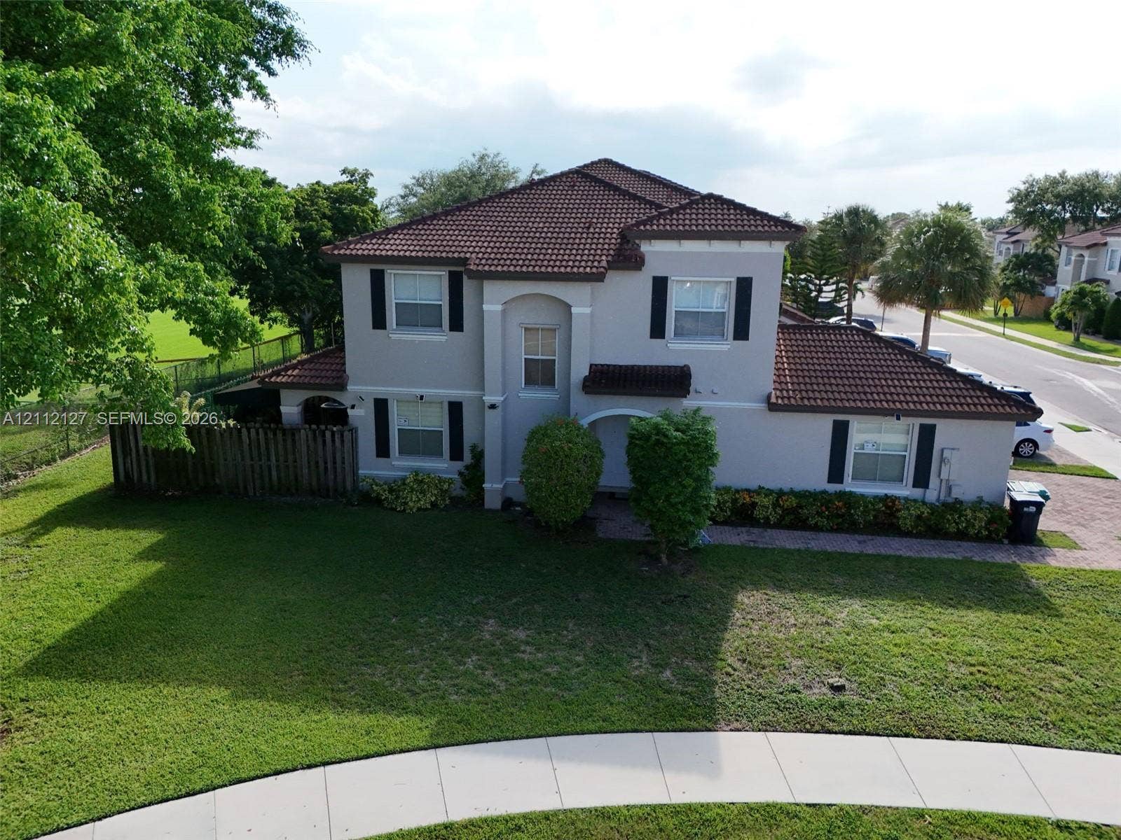 Two-story exterior featuring a tile roof, neutral stucco finish, decorative shutters, brick-paver driveway, and landscaped front yard