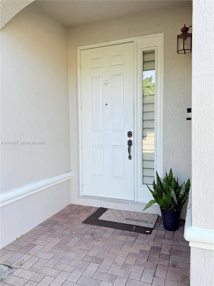 Covered entryway featuring a brick-paver porch, six-panel door with a sidelight, and an attached wall-mounted lantern fixture