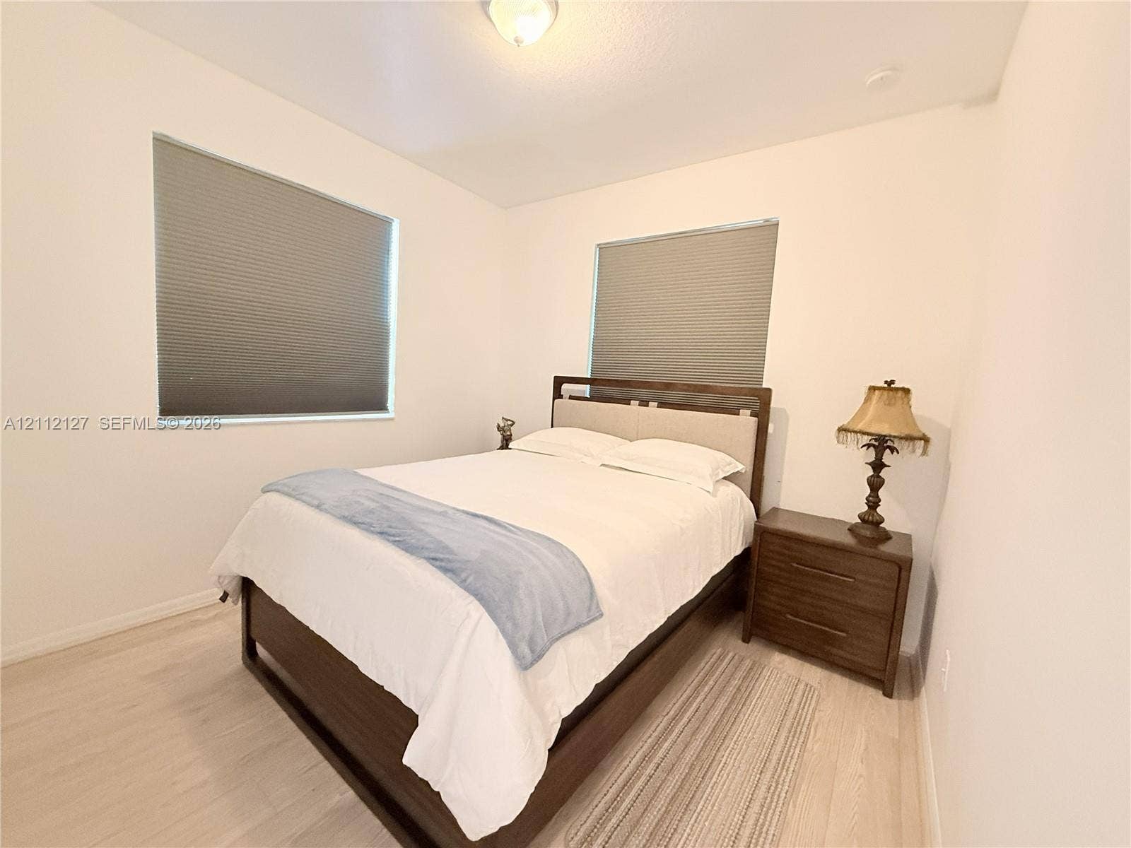 Neutral walls, light-toned wood-finish flooring, dual windows with fitted cellular shades, and a central ceiling-mounted light fixture